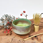 Ceramic bowl with green tea, bamboo whisk, and branches on a wooden surface