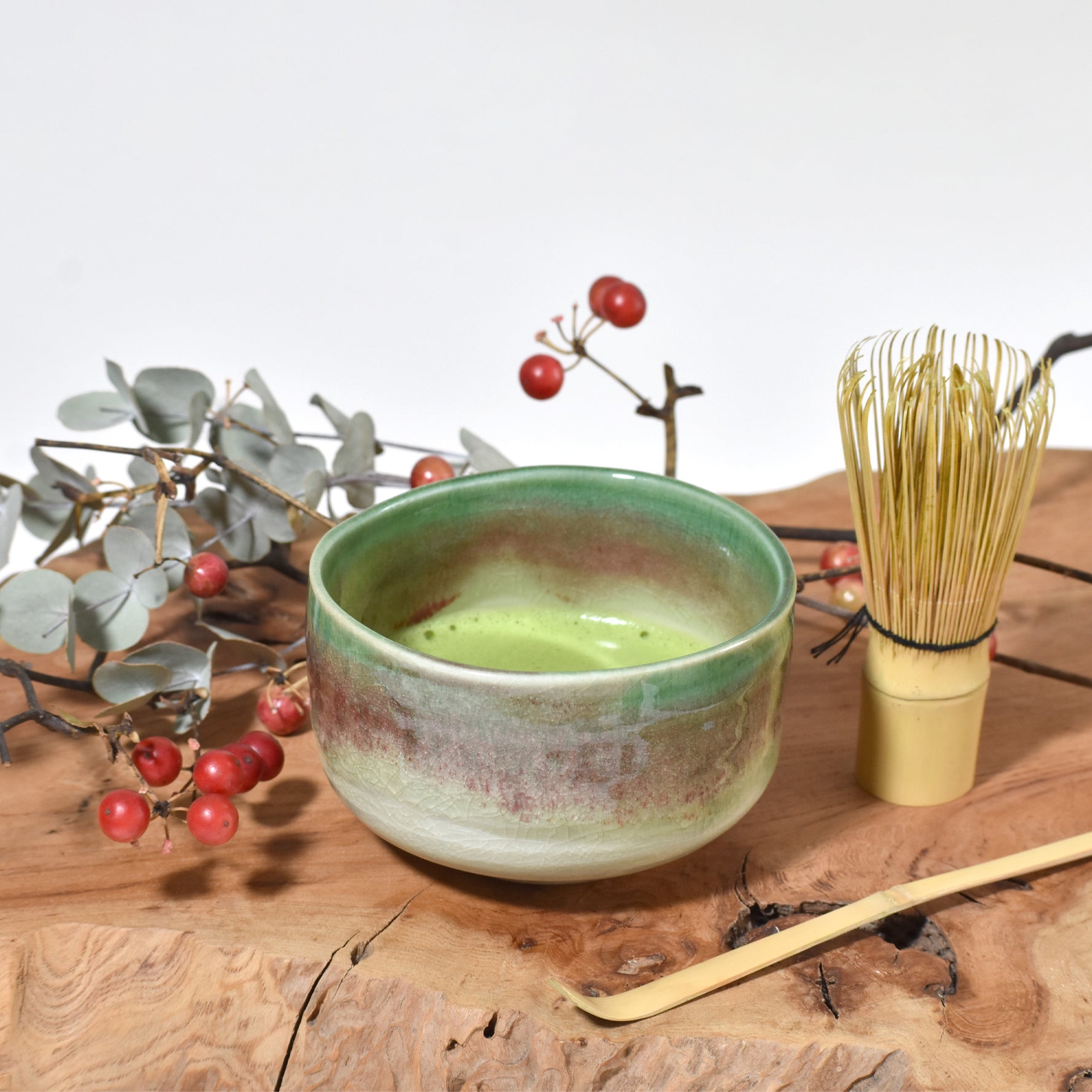 Ceramic bowl with green tea, bamboo whisk, and branches on a wooden surface