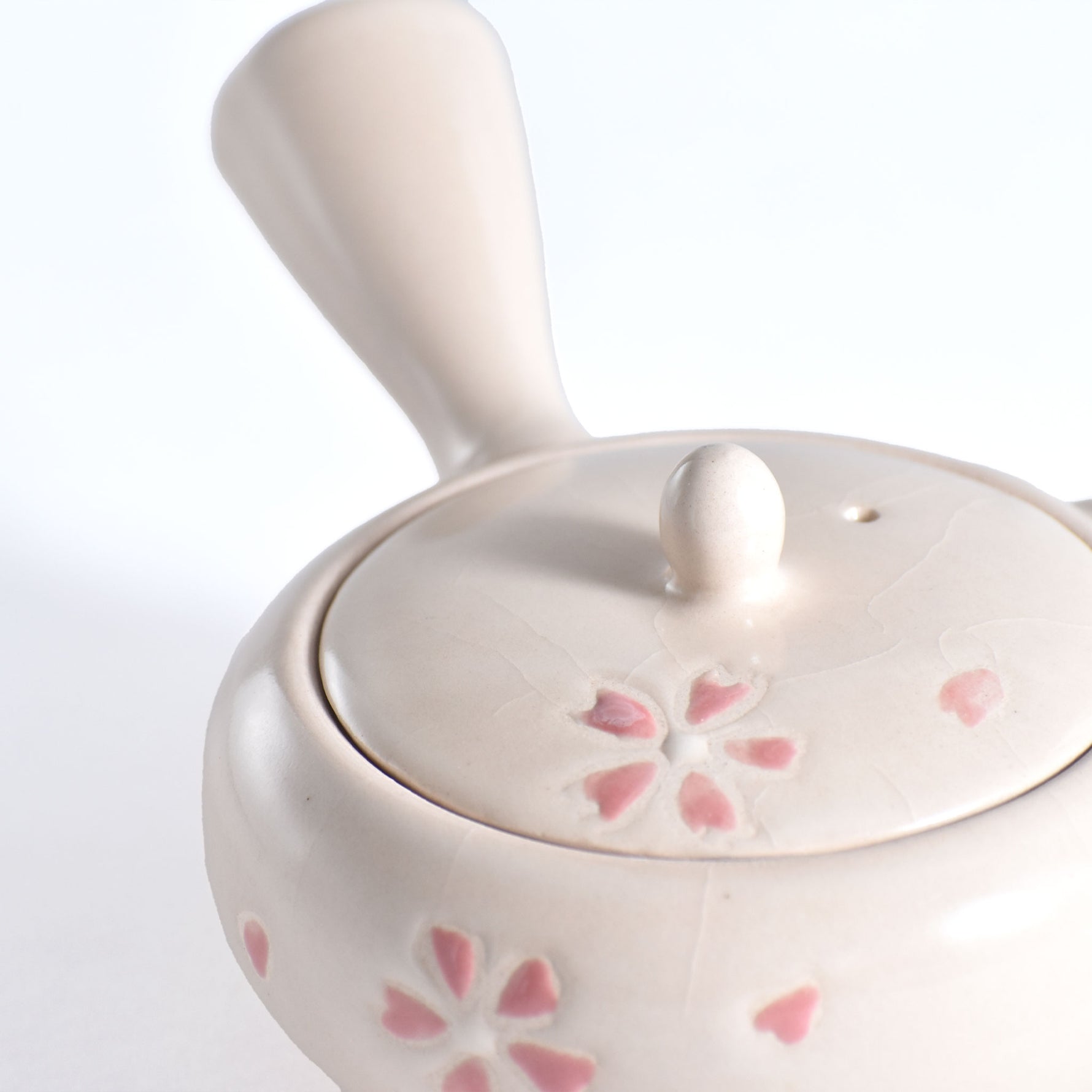 White ceramic teapot with pink floral patterns on a white background