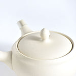 White ceramic teapot with lid on a light gray background