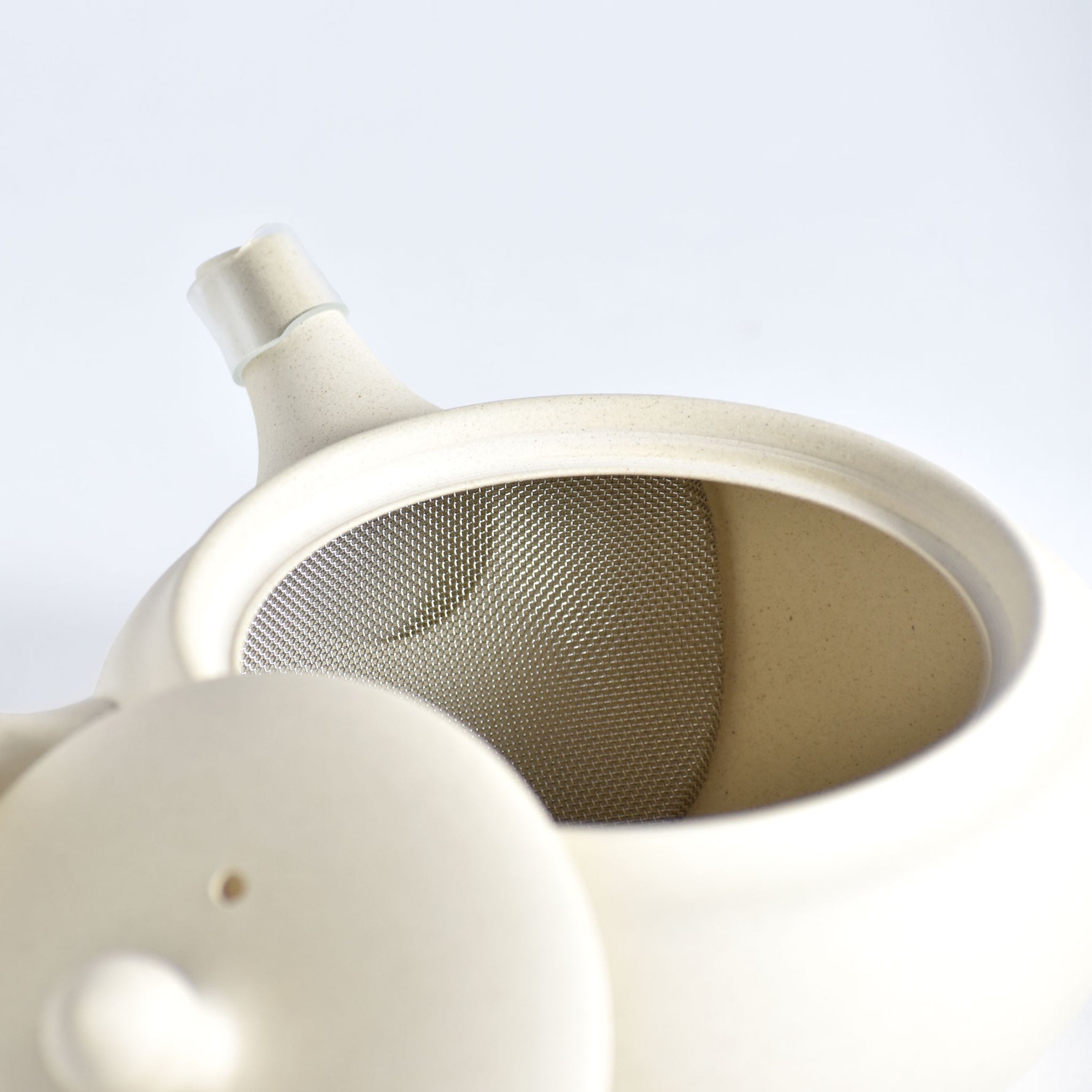 Close-up of a white ceramic teapot with a mesh filter on a light gray background