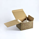 Open cardboard box with a patterned interior containing two white ceramic teapots on a light gray background