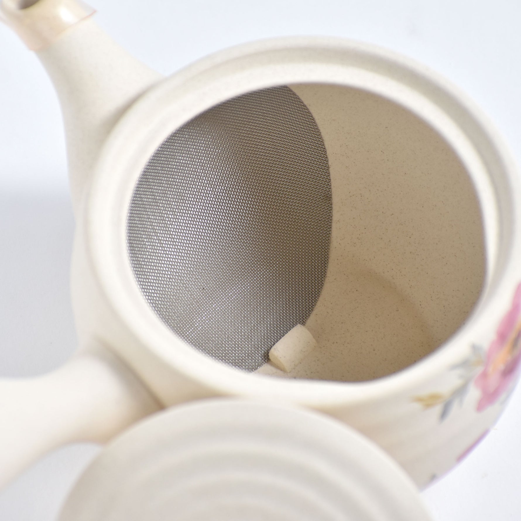 Close-up of a ceramic teapot with a metal tea infuser.