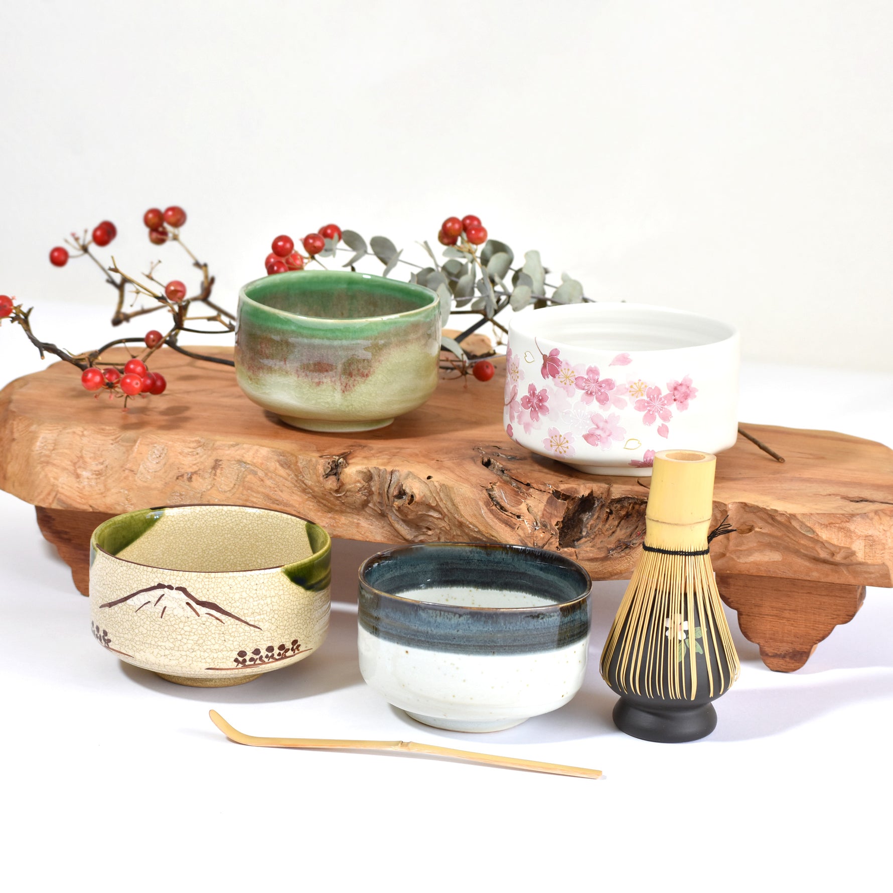 Set of ceramic tea cups and a whisk on a wooden stand with decorative branches.