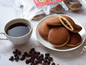 Cup of coffee with a plate of chocolate-filled cookies on a light surface.
