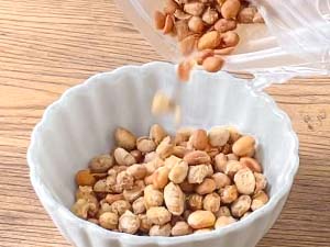 Natto being poured into a white bowl on a wooden surface