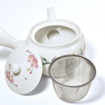 White ceramic teapot with floral design and metal mesh filter on a white background