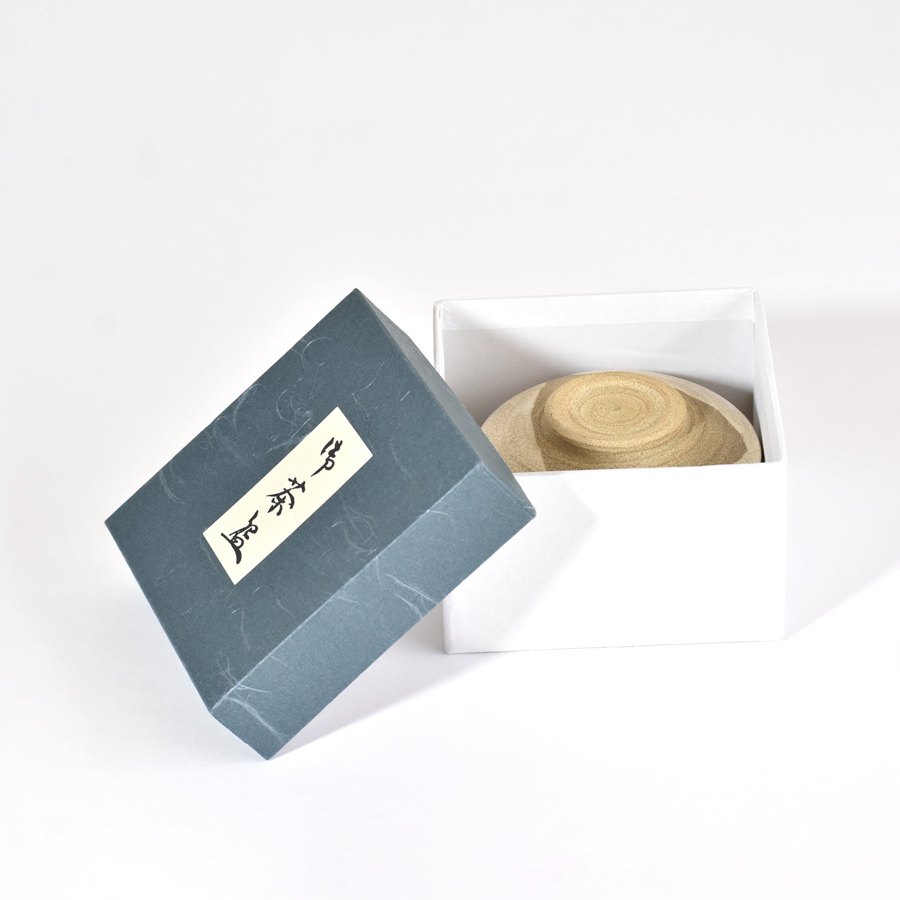 Blue box with a lid open, revealing a woven item inside on a white background