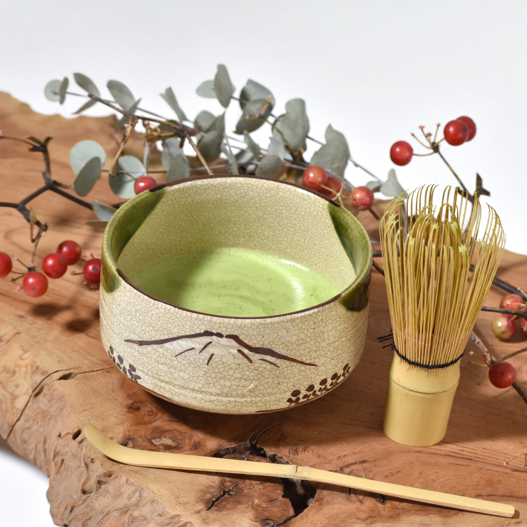 Green ceramic bowl with wooden whisk on a wooden surface with branches and berries