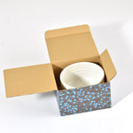 White ceramic bowl inside an open cardboard box with a floral pattern on a white background