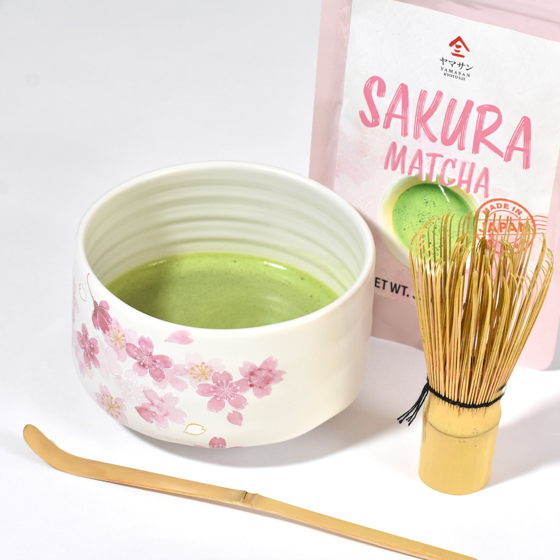 Matcha green tea set with a bowl, whisk, and Sakura Matcha packaging on a white background