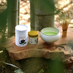 Matcha green tea set with containers and a bowl on a wooden surface with bamboo in the background