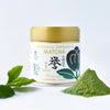 Container of Japanese Organic Matcha with matcha powder and leaves on a white background