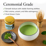 Ceremonial grade matcha with a bowl of green tea, whisk, and container on a wooden surface.