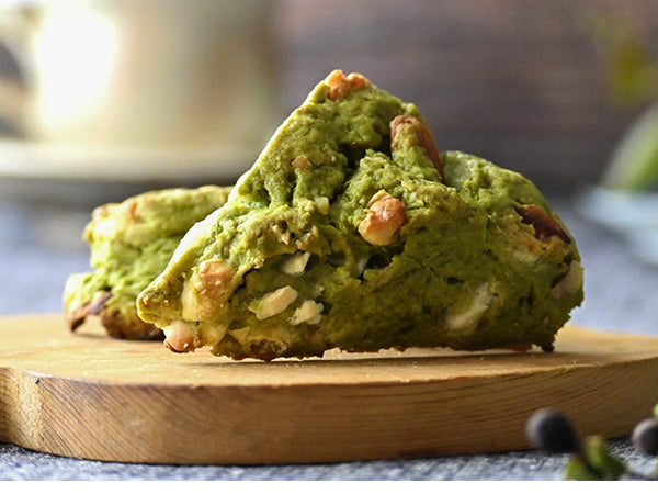 Two green savory scones filled with nuts and white cheese, served on a round wooden board.