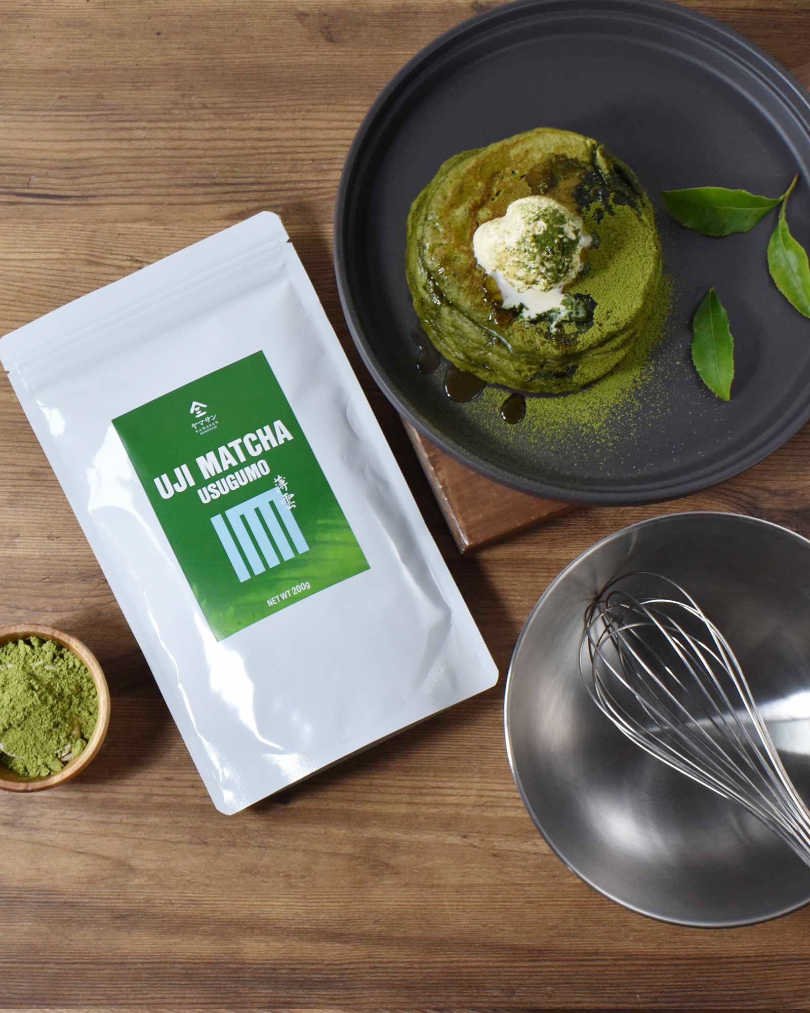 Uji Matcha Usugumo packaging with green matcha pancakes on a plate, bowl of matcha powder, and whisk on a wooden surface.