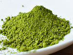 A close-up of bright green matcha powder piled on a white plate against a white background.