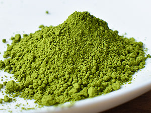 A close-up of bright green matcha powder piled on a white plate against a white background.