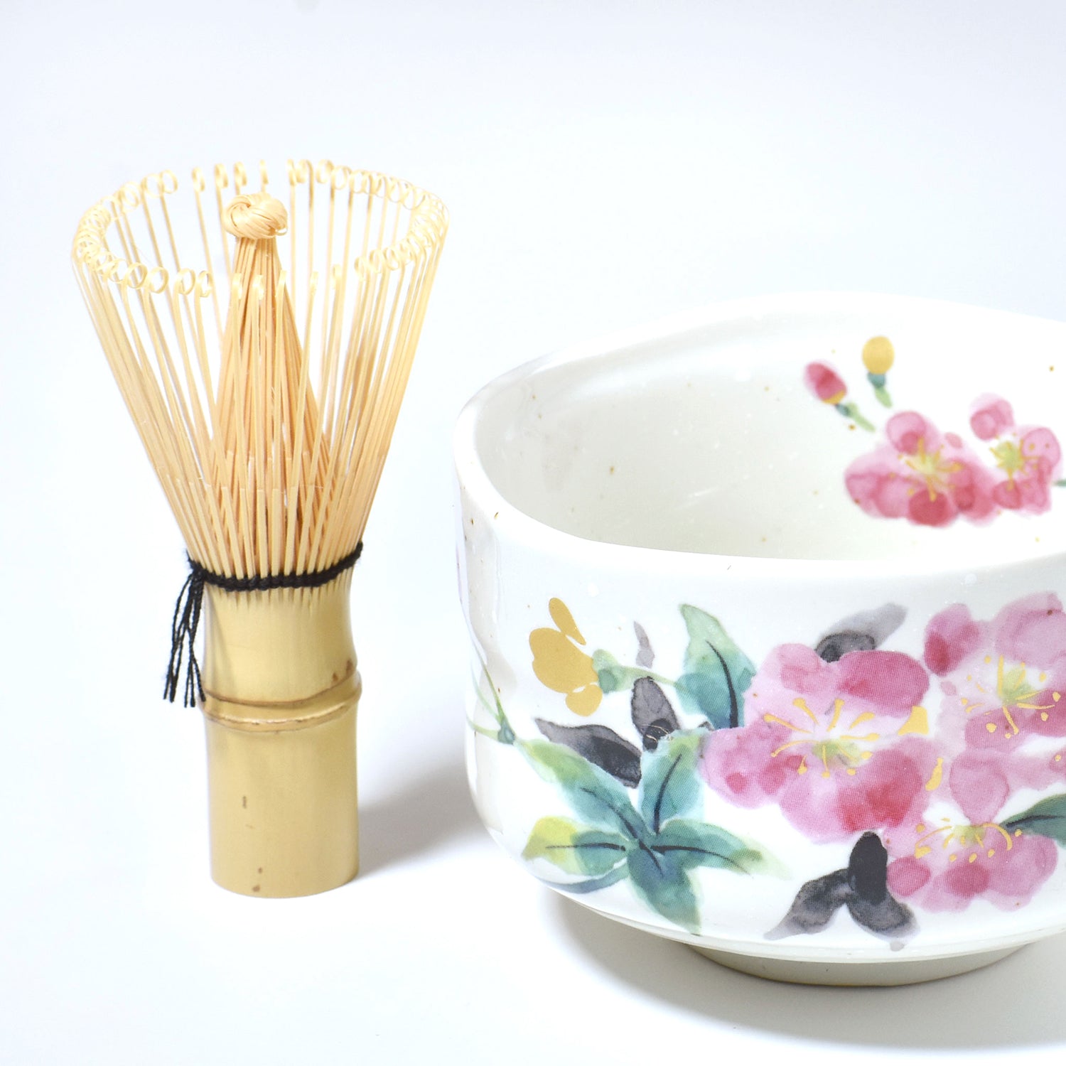 Bamboo whisk and ceramic bowl with floral design on a white background