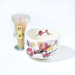 Matcha bowl with floral design and bamboo whisk on a white background