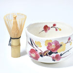 Ceramic bowl with floral design and bamboo whisk on a white background