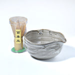 Gray ceramic matcha bowl and bamboo whisk set on a white backgroun