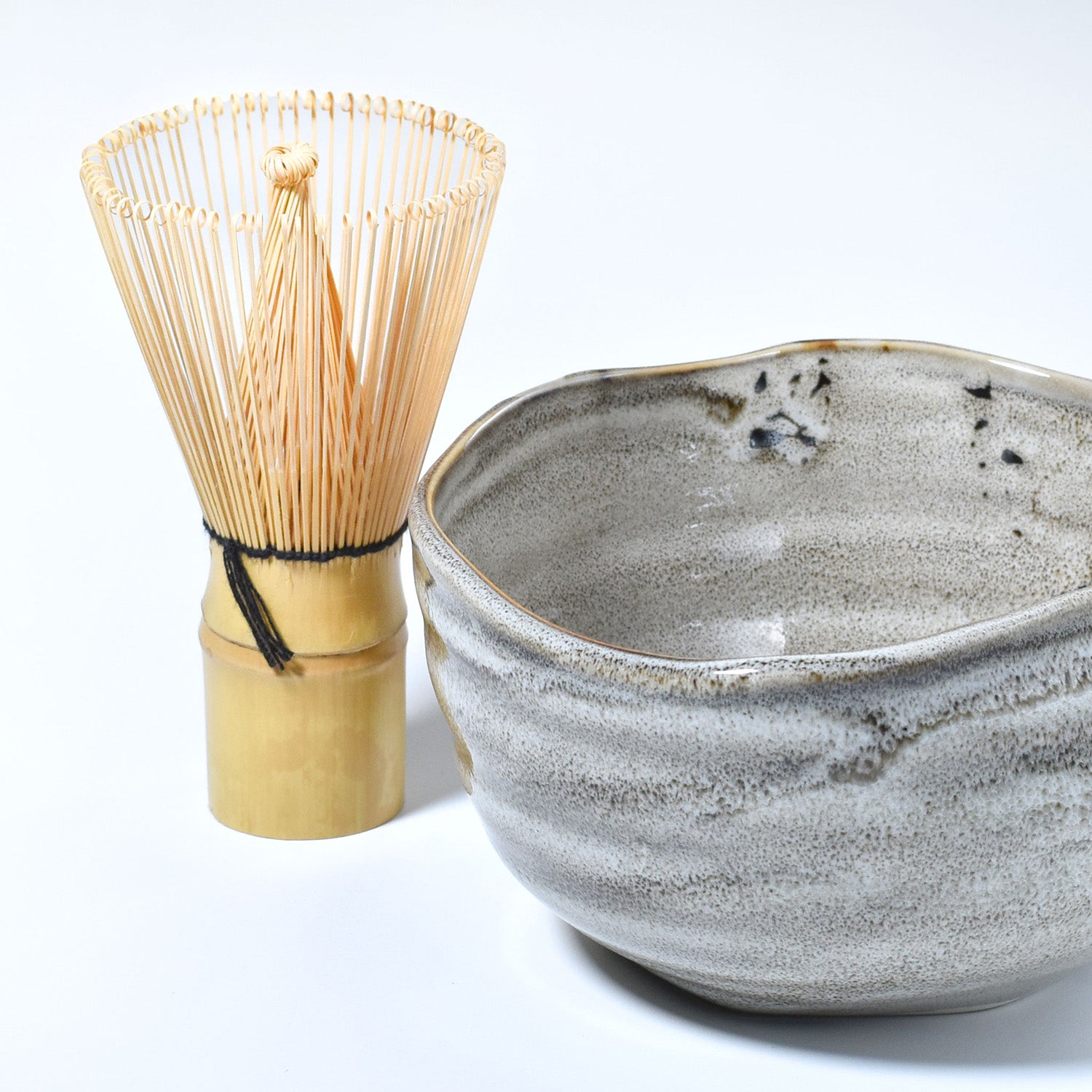 Gray ceramic matcha bowl and bamboo whisk set on a white backgroun