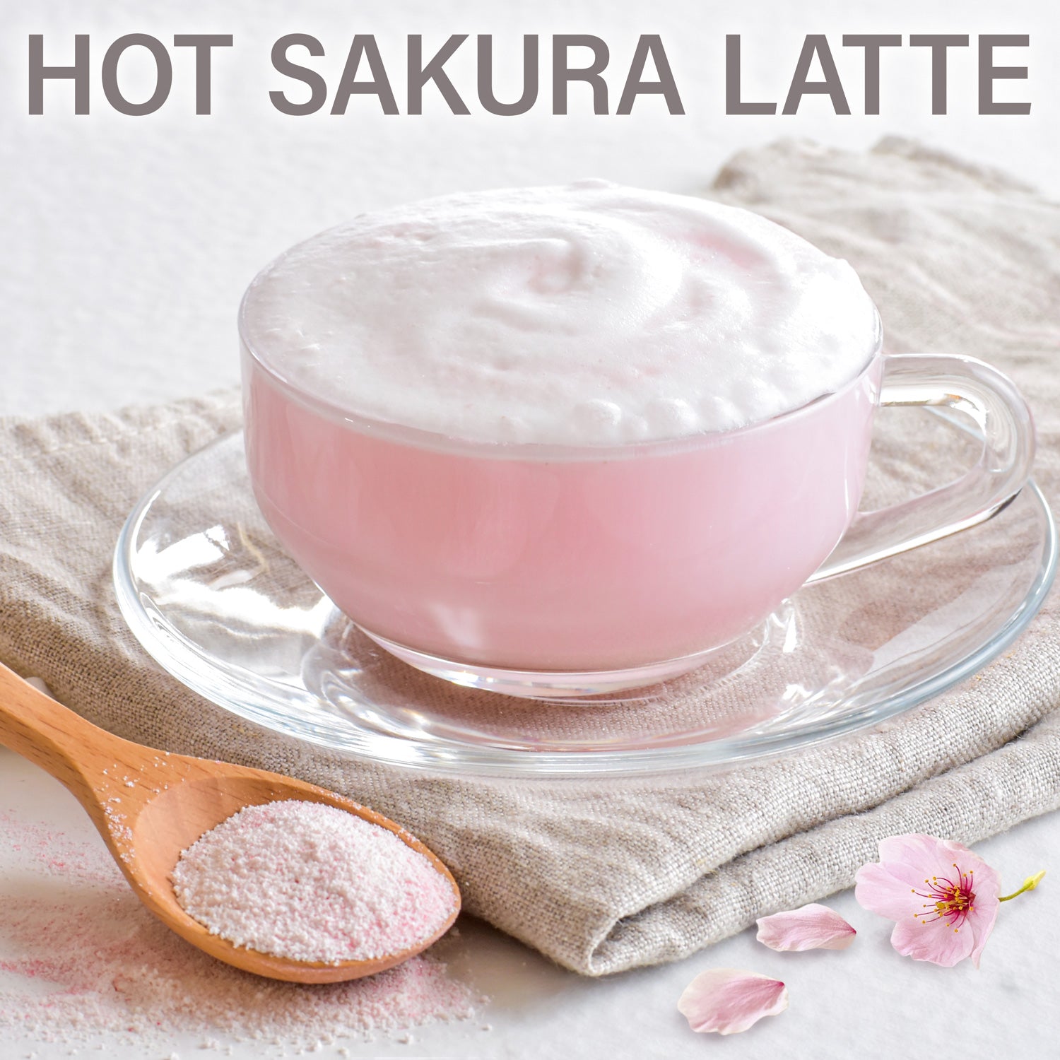 Hot Sakura Latte with a wooden spoon of pink powder and cherry blossom petals on a light background